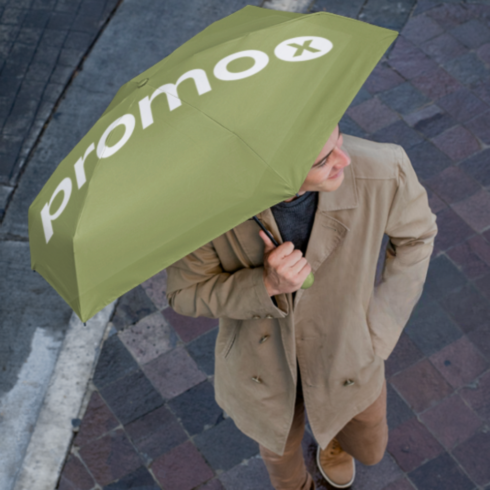 Foto av en ung man som håller ett grönt paraply med PromoX-logotypen i vitt